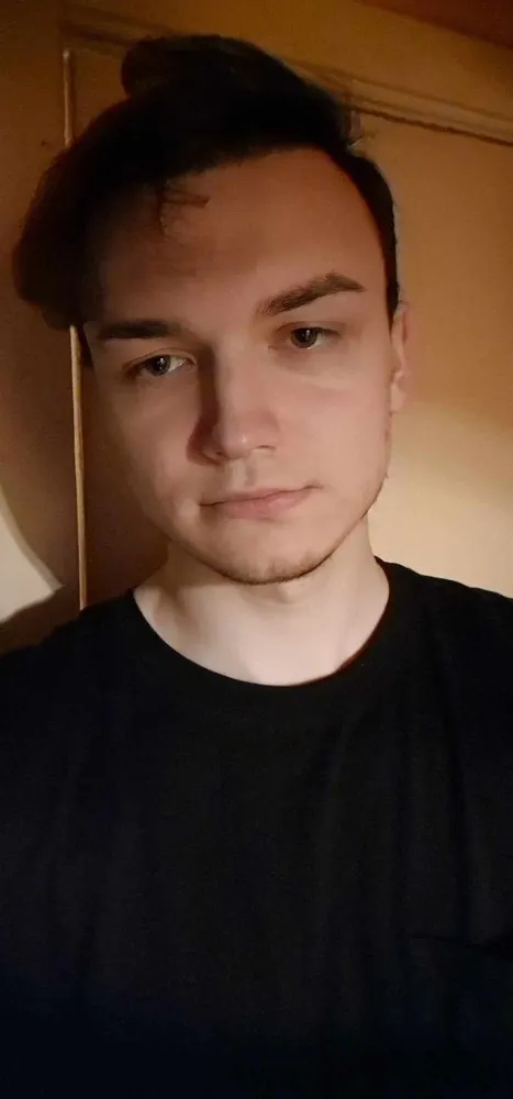 Photo of Yuozas in 2026 — dark hair, black t-shirt, warm low light
